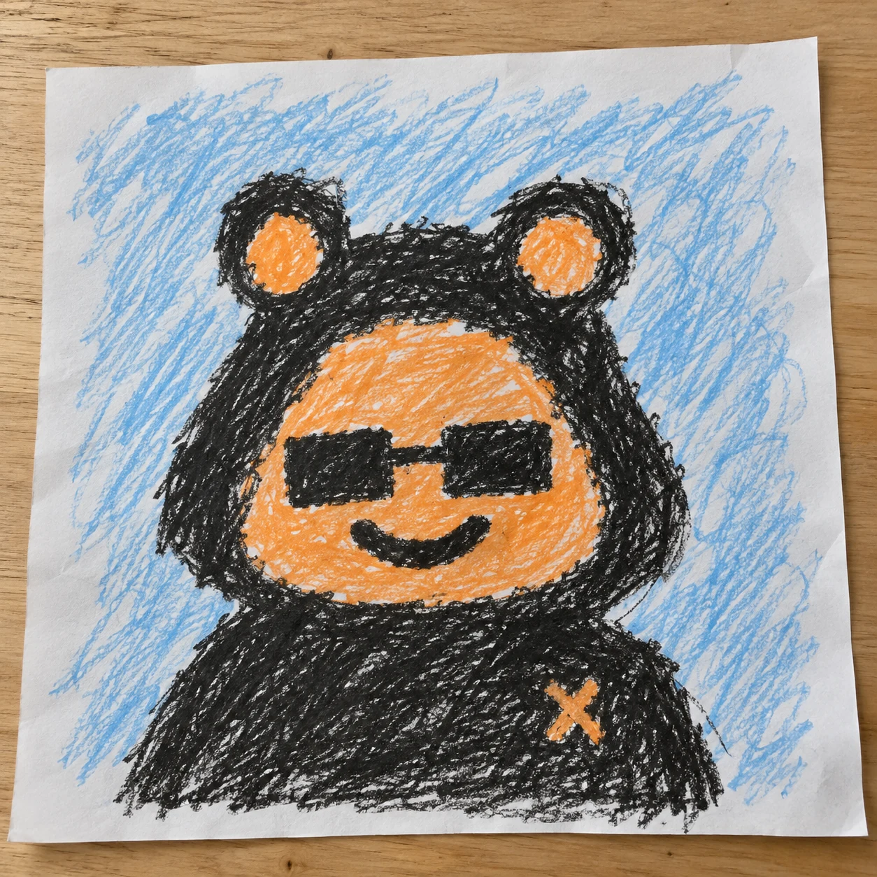An orange Crayon with bear ears and sunglasses, drawn on blue-scribbled paper on a wooden table