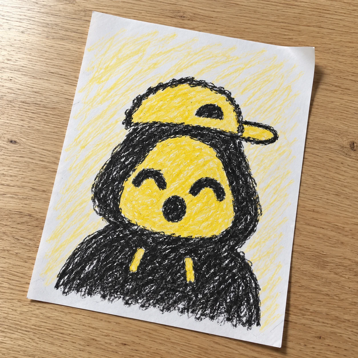 A happy yellow Crayon wearing a cap, drawn on yellow-scribbled paper on a wooden table
